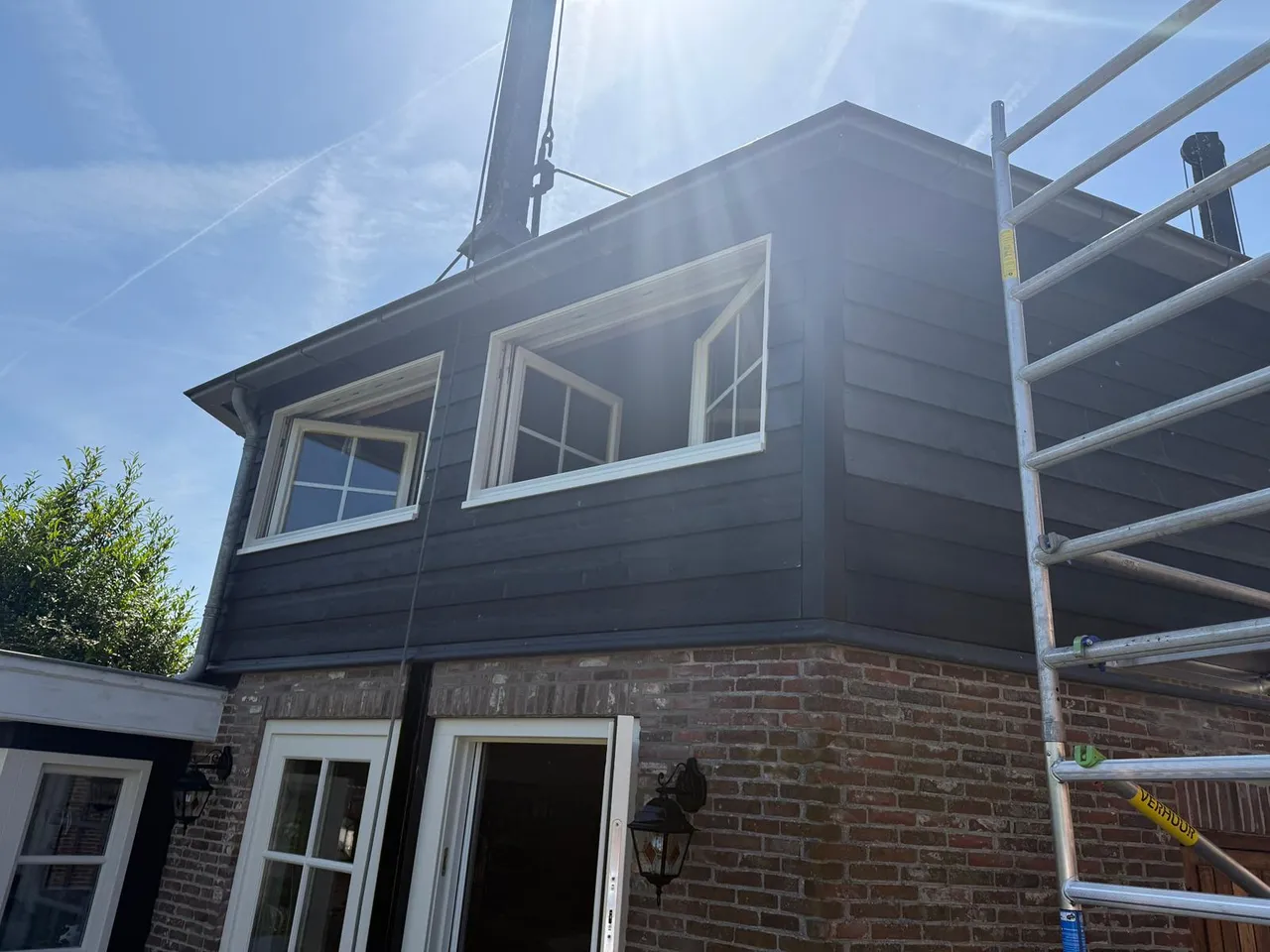Antracietgrijze houten bovengevel op een bakstenen onderbouw met witte kozijnen
