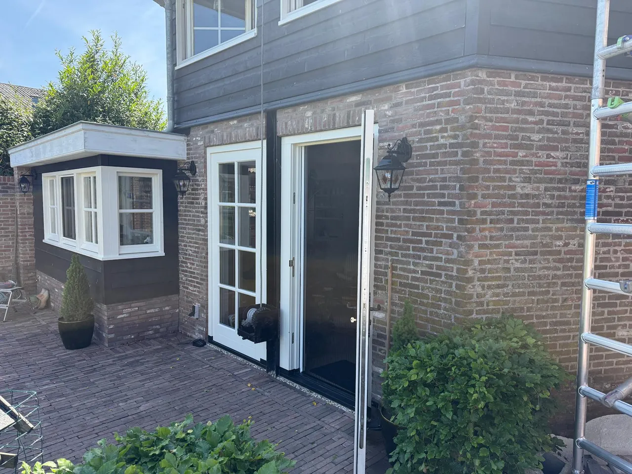 Bakstenen gevel met witte erker en crème openslaande tuindeuren na schilderwerk