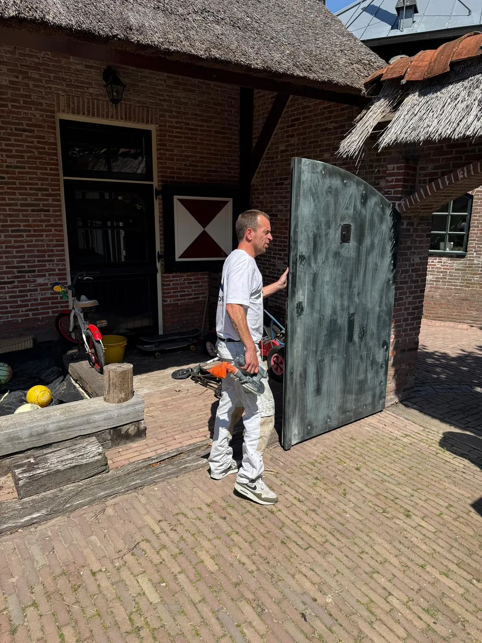 Schilder draagt een grote houten poort tijdens renovatie bij een rieten schuur