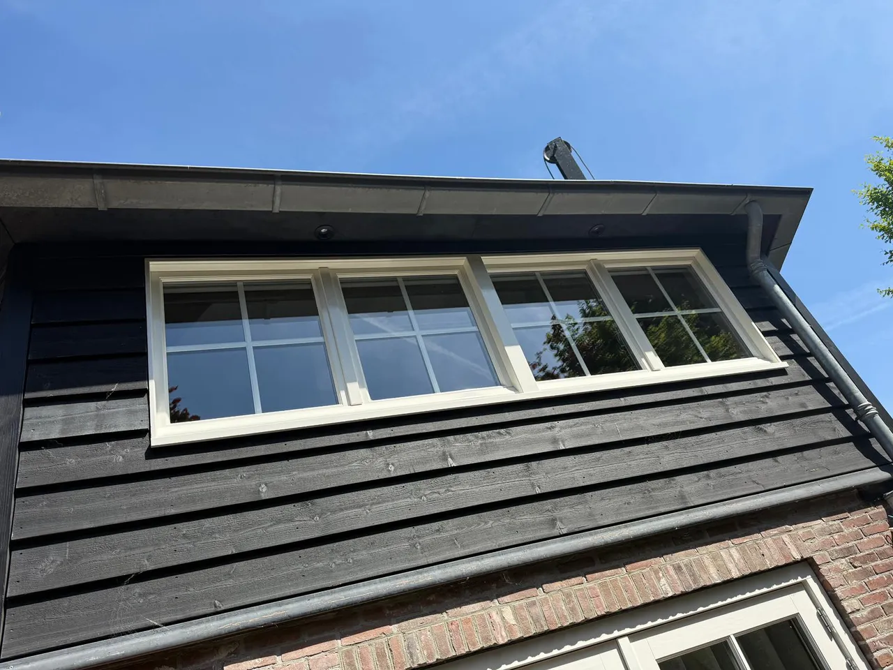 Witte kozijnen in een zwarte houten topgevel tegen een blauwe lucht